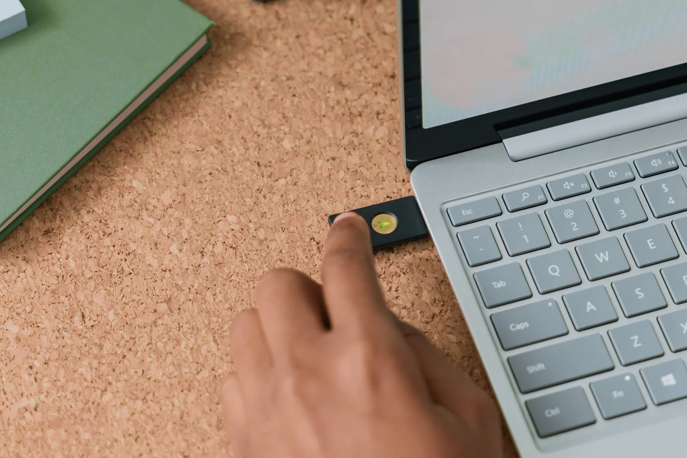 Prst dodiruje YubiKey utaknut u bočni priključak prijenosnika na plutenom stolu