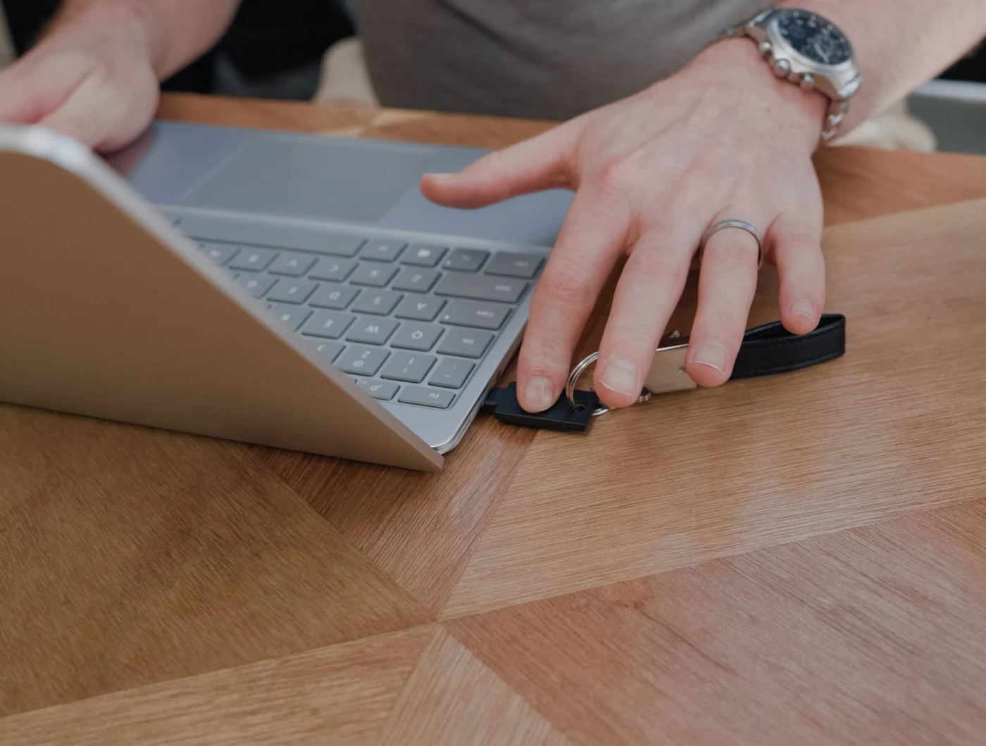 Ruka dodiruje sigurnosni ključ YubiKey na privjesku, umetnut u prijenosnik na drvenom stolu