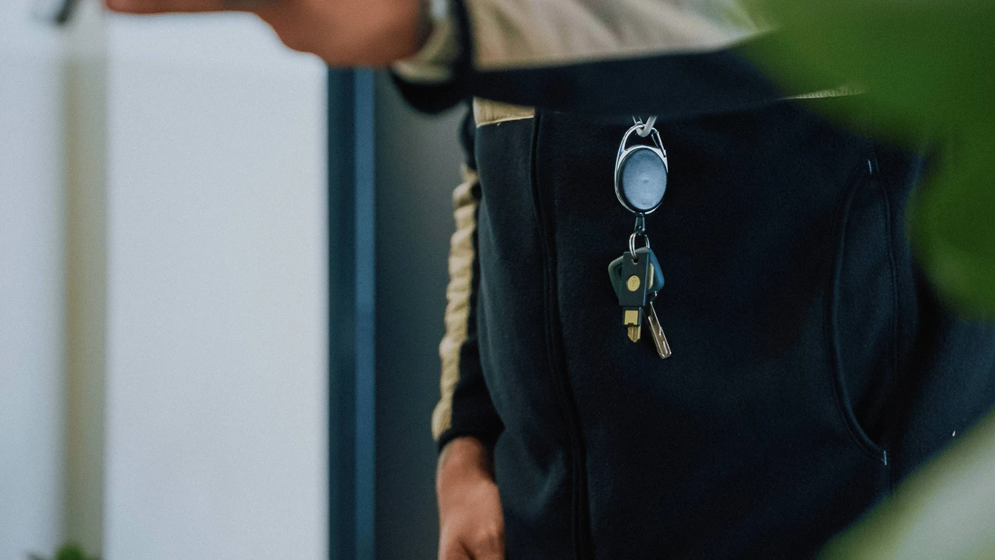 Sigurnosni ključ YubiKey i obični ključ na rastezljivom držaču zakačenom za tamnu radnu odjeću