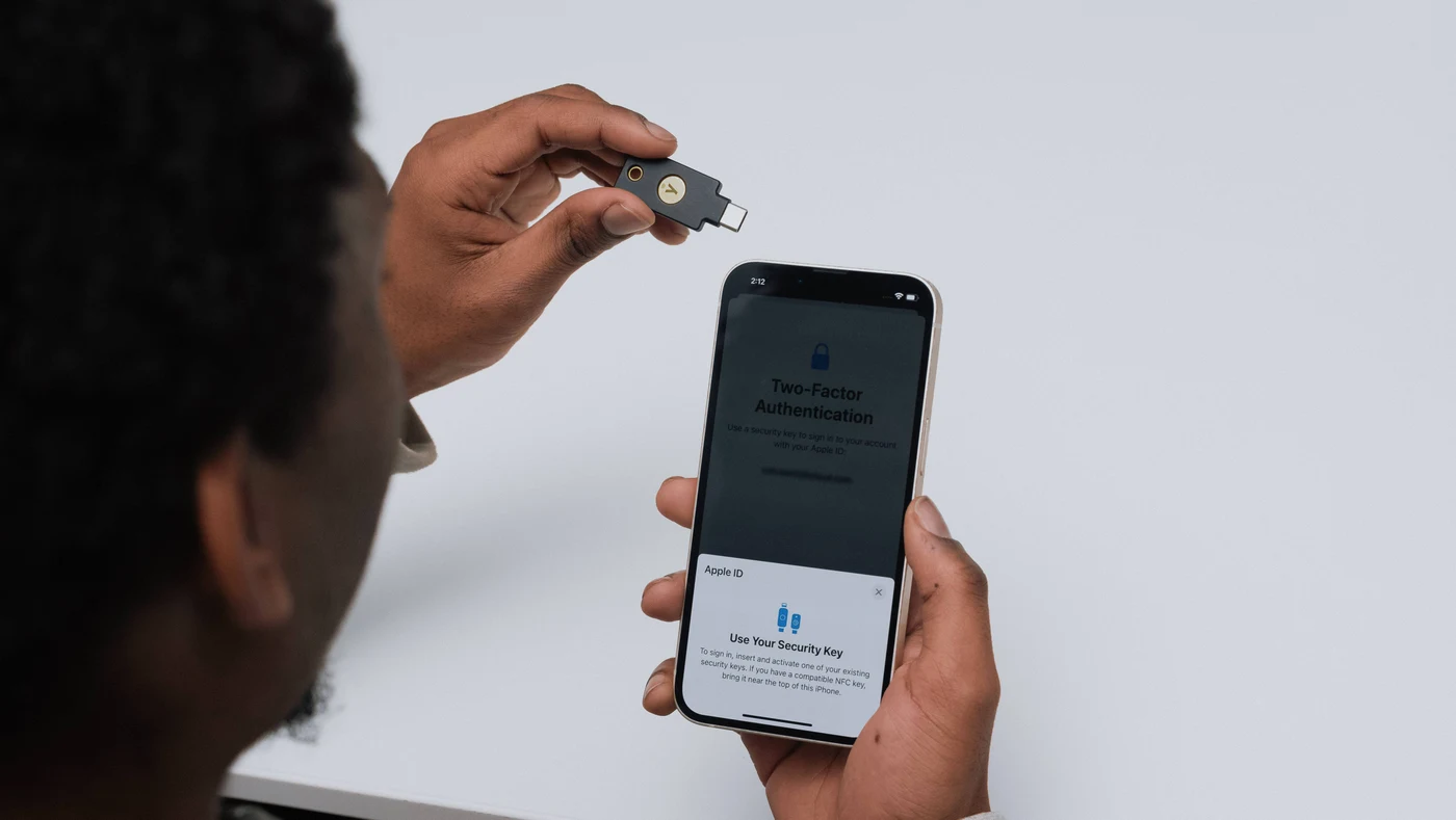 Osoba drži YubiKey 5C NFC iznad iPhonea na kojem Apple ID traži sigurnosni ključ za prijavu