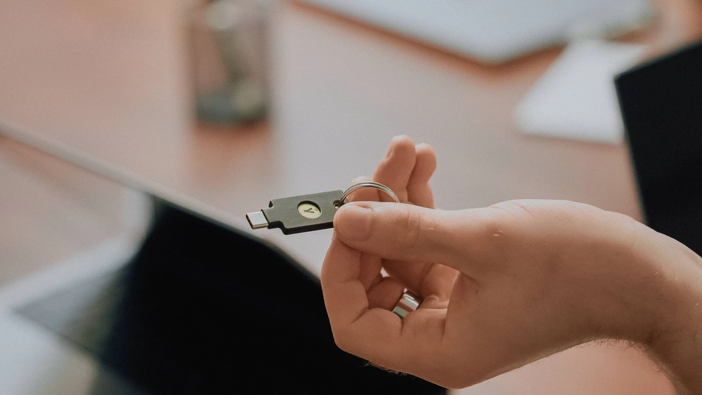 Ruka drži sigurnosni ključ YubiKey 5C NFC na privjesku; na ključu je samo logotip, bez imena i podataka