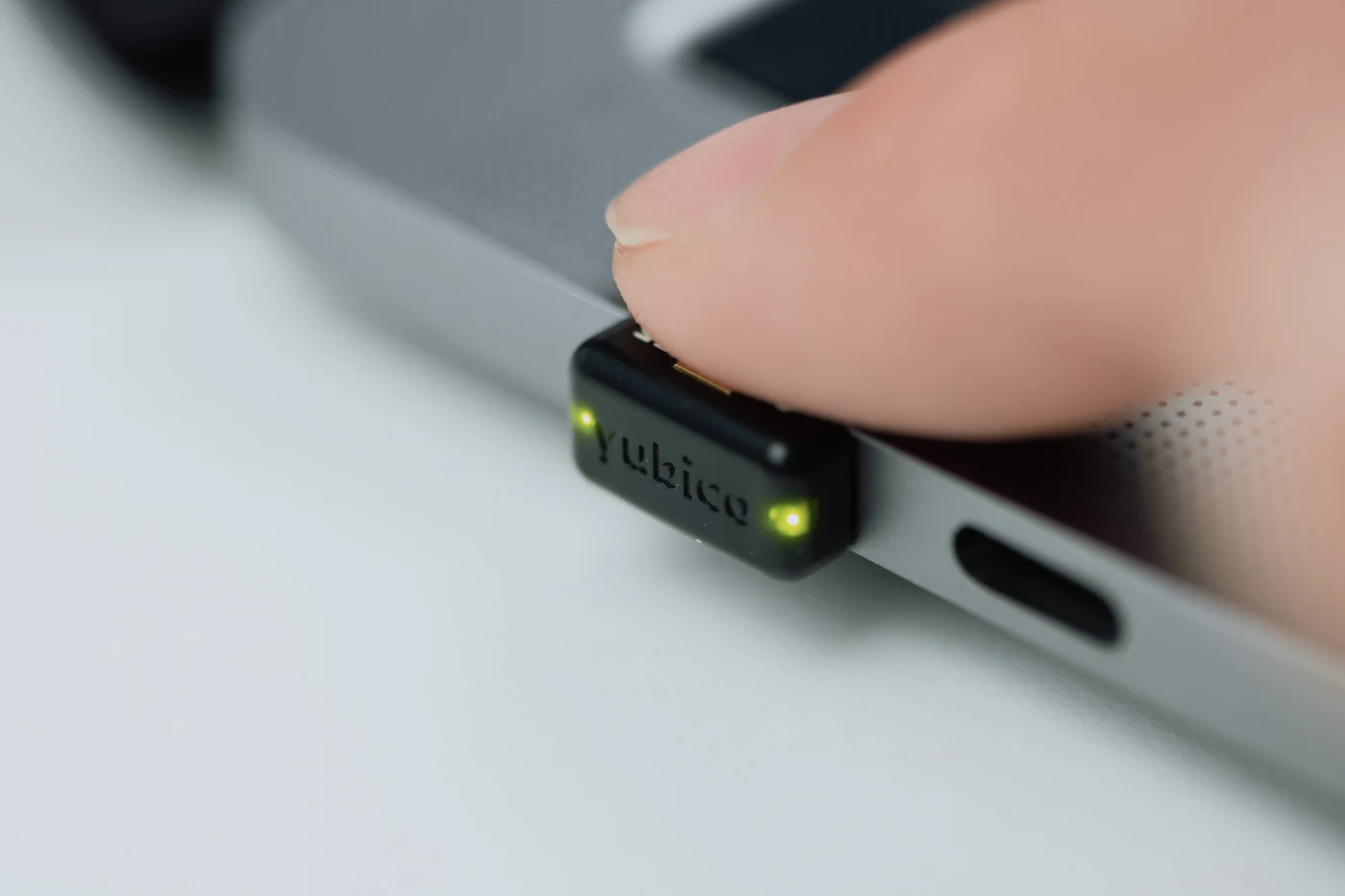 Prst dodiruje YubiKey Nano umetnut u USB-C priključak prijenosnika, uz upaljene lampice na ključu