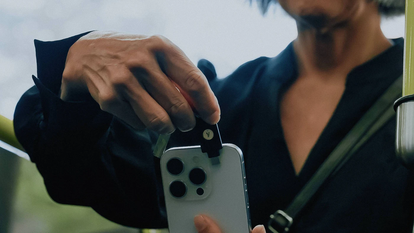 Osoba u javnom prijevozu prislanja YubiKey s privjeskom uz gornji rub iPhonea