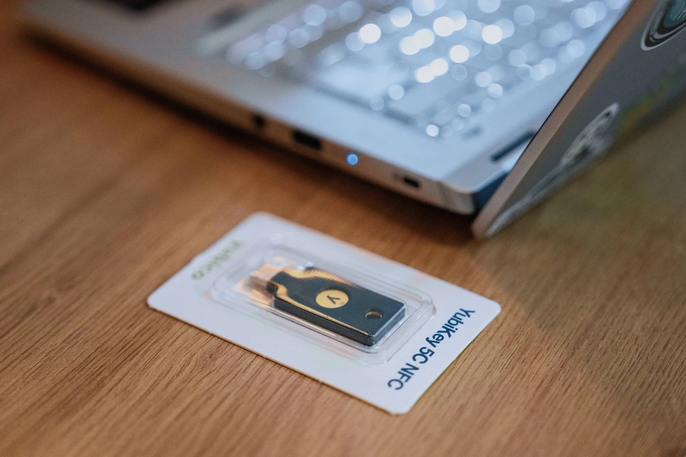YubiKey 5C NFC u originalnom pakiranju na drvenom stolu, pokraj USB-C priključka prijenosnika