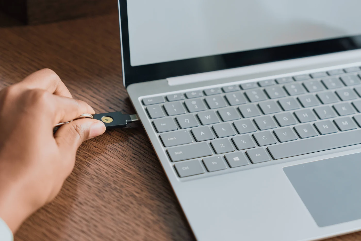 Ruka umeće sigurnosni ključ YubiKey s USB-C priključkom u prijenosnik na drvenom stolu
